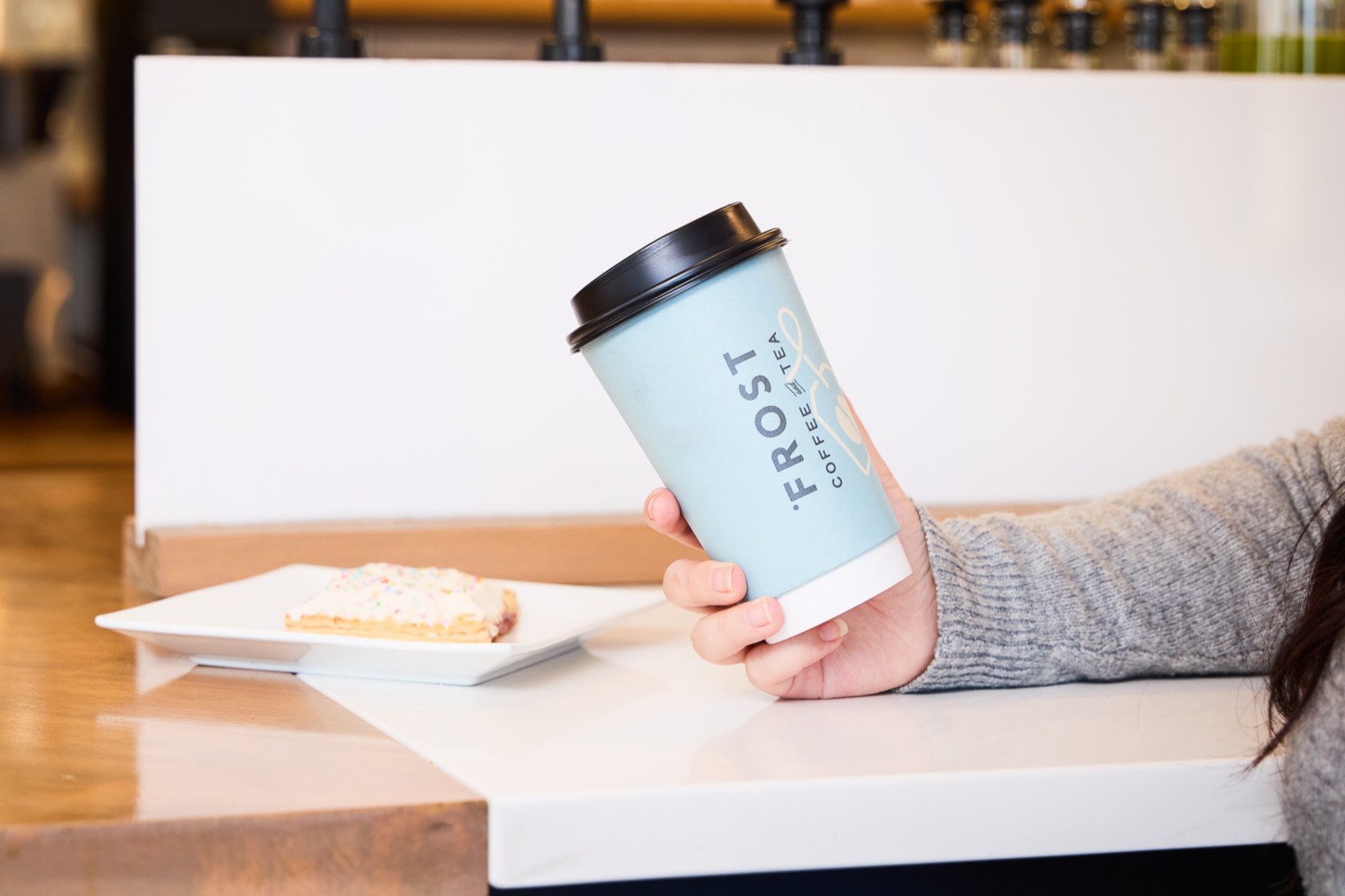 image of somebody holding a blue paper coffee cup and a plate with a baked pastry